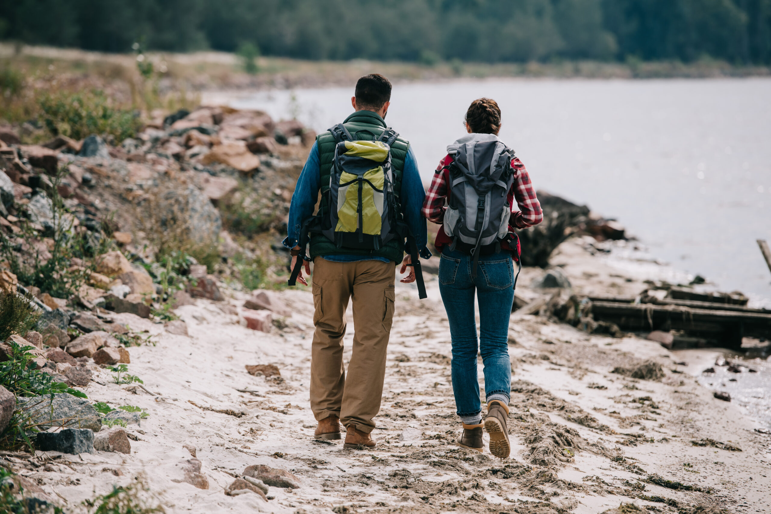back view of hikers with backpacks walking on sandy beach together